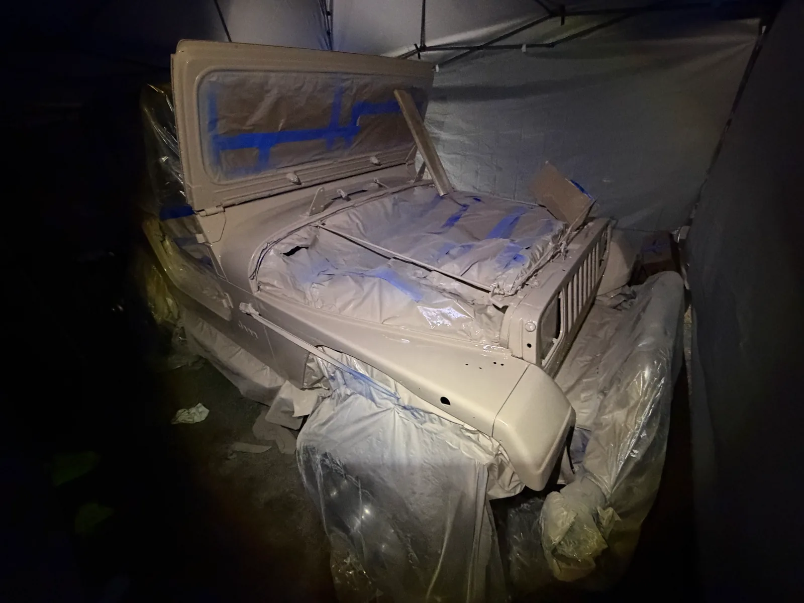 The tan Jeep with front end masked during reassembly