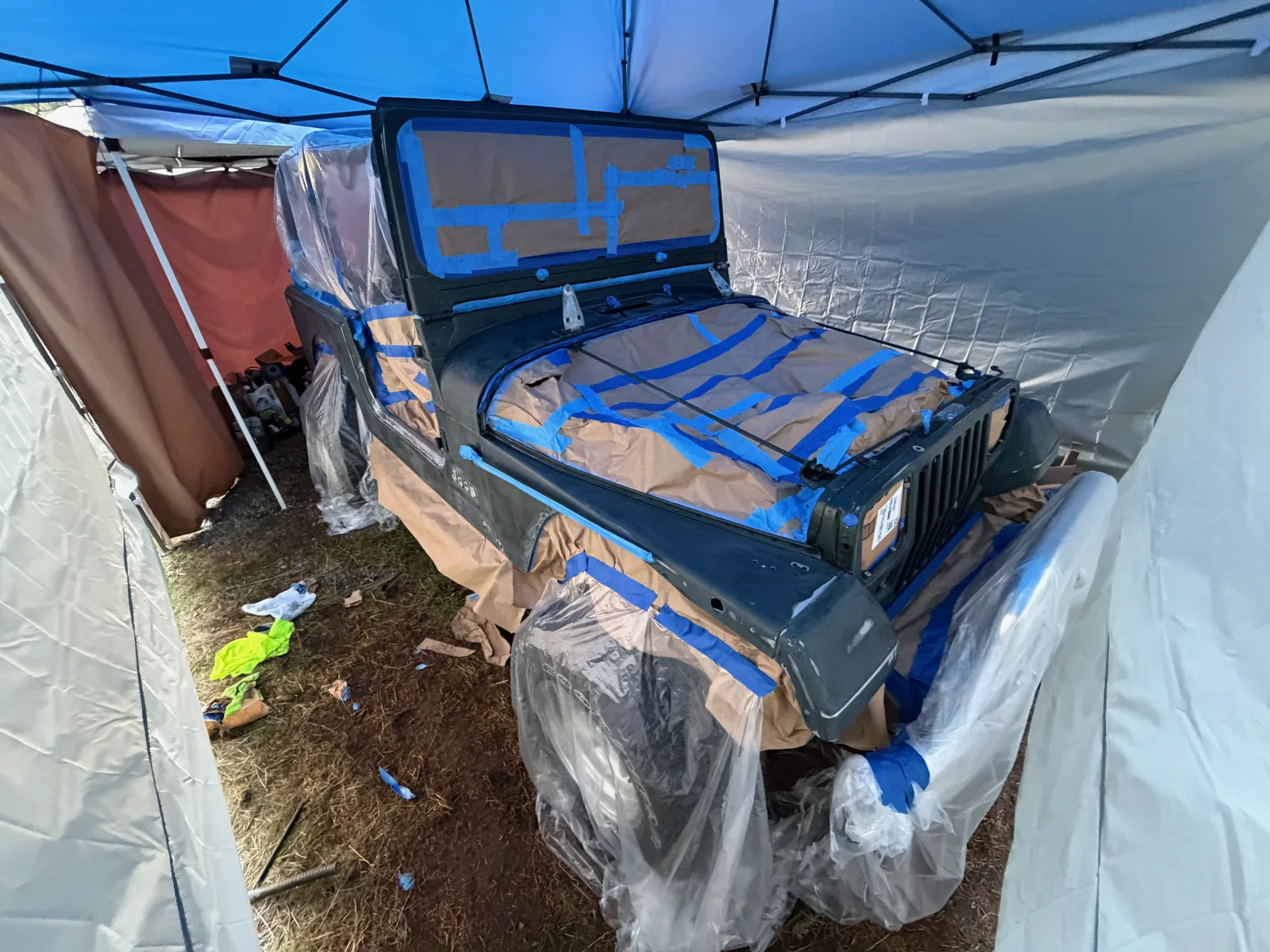 The Jeep masked with blue tape under a pop-up canopy